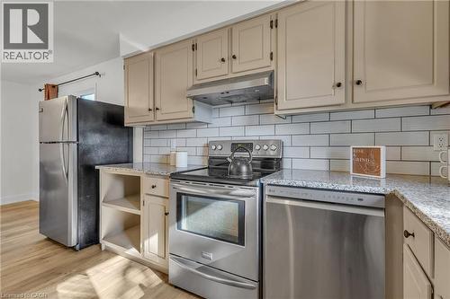 Kitchen featuring cream-colored cabinetry, light-toned granite countertops, a white subway tile backsplash, stainless steel appliances, and wood-finish flooring - 127 Acorn Crescent, London, ON 