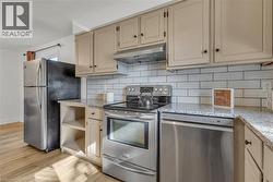 Kitchen featuring cream-colored cabinetry, light-toned granite countertops, a white subway tile backsplash, stainless steel appliances, and wood-finish flooring - 