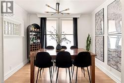 Dining area featuring light wood-finish flooring, white crown molding, and two windows with dark drapery - 