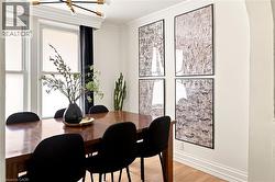 Dining area featuring a wood-finish table, multiple windows with roller shades, and a modern chandelier with gold-tone accents - 