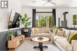 Living area featuring wood-finish flooring, a ceiling fan, and a wood stove with exposed piping - 