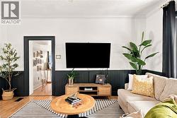 Living area featuring wood-finish flooring, a decorative area rug, and a dark accent wainscoting - 