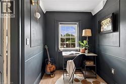 Room featuring deep-toned wainscoting and crown molding, wood-finish flooring, a single hung window, and a modern wall sconce with a spherical globe - 