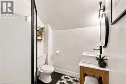 Compact bathroom featuring a frosted glass shower enclosure with a black frame, hexagonal floor tiling, a wood-finish vanity with a vessel sink, a black wall-mounted faucet, and a circular black-frame - 