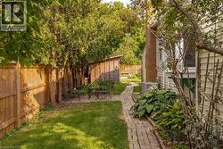 Expansive backyard featuring a brick paver pathway, a dedicated patio area, a storage shed, wood privacy fencing, and mature perimeter landscaping - 