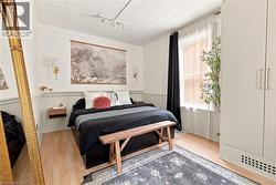 Bedroom with wood-finish flooring, white paneled walls, and track lighting - 