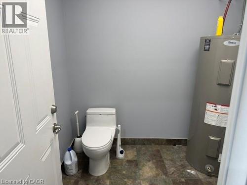 Restroom featuring a white toilet with a closed-lid design, light gray walls, and dark-toned tile flooring - 95 Hempstead Drive Unit# 9, Hamilton, ON 
