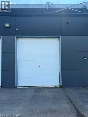 White sectional overhead door set into a dark gray facade with an asphalt parking surface - 95 Hempstead Drive Unit# 9, Hamilton, ON 