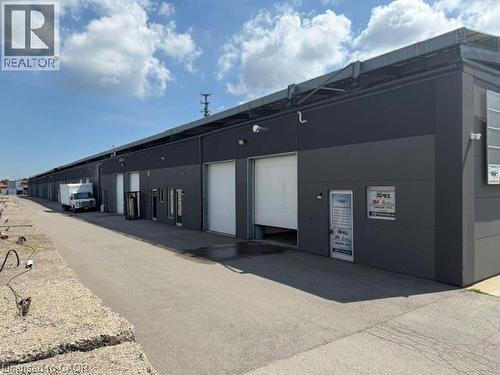 Modern commercial building featuring dark gray paneling, multiple white roll-up garage doors, individual entry doors, and exterior lighting fixtures - 95 Hempstead Drive Unit# 9, Hamilton, ON 