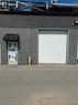 Commercial building featuring a roll-up garage door, pedestrian entrance with awning, exterior lighting, and security camera - 95 Hempstead Drive Unit# 9, Hamilton, ON 