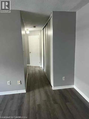 Hallway featuring dark wood-finish flooring, light grey painted walls, white baseboards, and a series of sliding closet doors - 529 Parkside Drive Unit# 7, Waterloo, ON 