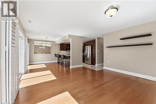 Spacious living area featuring wood-finish flooring, white plantation shutters, and a recessed kitchen with dark wood cabinetry and stainless steel appliances - 29 Archdeacon Clark Trail, Hamilton, ON 