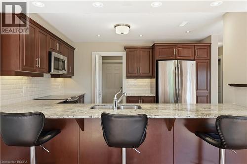 Kitchen featuring a granite-look island, stainless steel sink with a high-arc faucet, rich wood cabinetry, stainless steel appliances, and subway tile backsplash - 29 Archdeacon Clark Trail, Hamilton, ON 