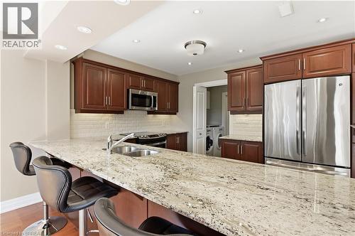 Kitchen featuring an expansive stone countertop with an undermount double-basin sink, rich wood cabinetry, stainless steel appliances, and subway tile backsplash - 29 Archdeacon Clark Trail, Hamilton, ON 