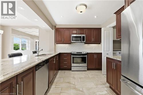 Kitchen featuring light-toned tile flooring, rich wood cabinetry, stainless steel appliances, and a light-toned countertop - 29 Archdeacon Clark Trail, Hamilton, ON 