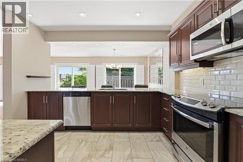 Kitchen featuring wood-finish cabinetry, granite countertops, and stainless steel appliances including a built-in microwave, dishwasher, and range - 29 Archdeacon Clark Trail, Hamilton, ON 
