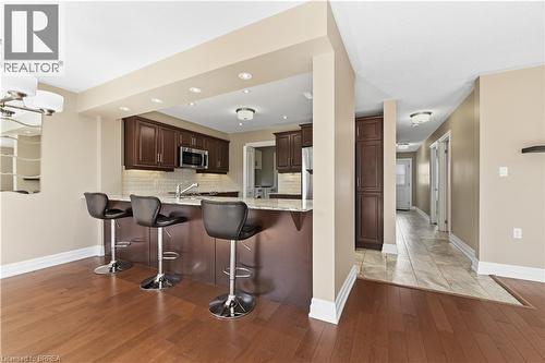 Kitchen featuring a breakfast bar with seating, wood-finish flooring, recessed lighting, stainless steel appliances, and dark wood cabinetry - 29 Archdeacon Clark Trail, Hamilton, ON 
