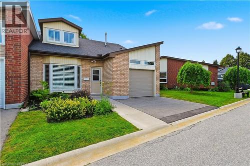 Brick facade residence featuring an attached garage with a paved driveway, a dormer window, and front landscaping - 29 Archdeacon Clark Trail, Hamilton, ON 