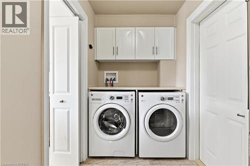 Dedicated laundry area featuring front-loading appliances, a neutral-toned countertop, and white upper cabinetry - 29 Archdeacon Clark Trail, Hamilton, ON 