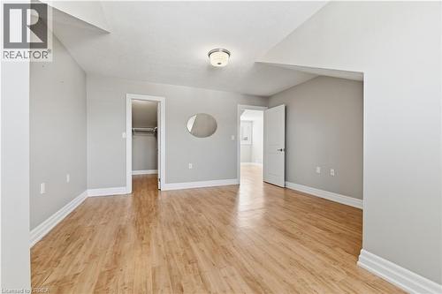 Spacious bedroom featuring wood-finish flooring, light gray wall paint, white trim, and a flush mount ceiling light fixture - 29 Archdeacon Clark Trail, Hamilton, ON 