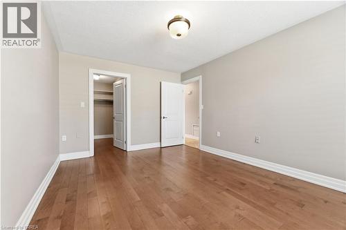 Spacious room featuring wood-finish flooring, light grey walls, white trim, and a ceiling-mounted light fixture - 29 Archdeacon Clark Trail, Hamilton, ON 