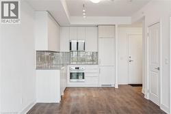 Contemporary kitchen featuring light wood-finish cabinetry, stainless steel appliances, a grey tile backsplash, and a double basin sink with a gooseneck faucet - 