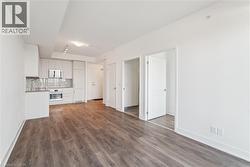 Open-concept living space featuring wood-finish flooring, a contemporary kitchen with light cabinetry, stainless steel appliances, and a tiled backsplash, along with multiple interior doorways - 