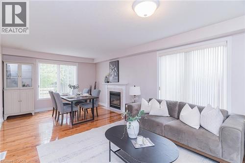 Open-concept living space featuring wood-finish flooring, a white fireplace with a tiled surround, a large window with vertical blinds, and a built-in display cabinet with glass doors - 566 Avignon Place, Waterloo, ON 