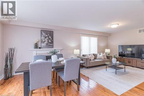 Open concept living and dining area featuring wood-finish flooring, a built-in fireplace mantel, and large windows with privacy blinds - 566 Avignon Place, Waterloo, ON 