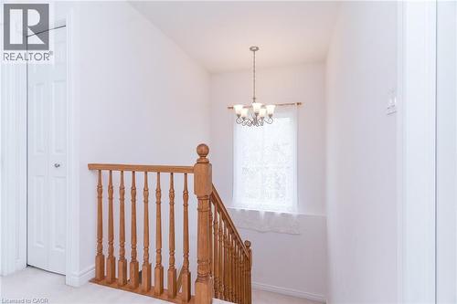 Hardwood staircase with turned balusters and newel post, illuminated by a multi-bulb pendant light fixture - 566 Avignon Place, Waterloo, ON 