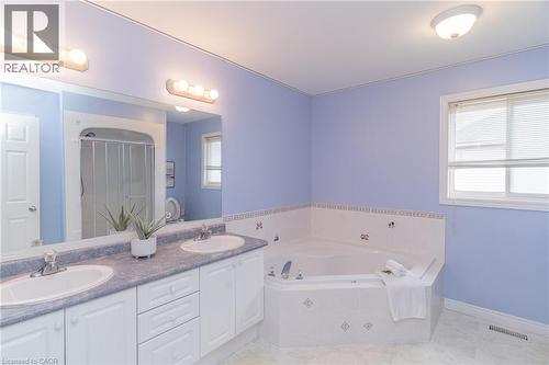 Bathroom featuring a built-in corner soaking tub, a dual vanity with undermount sinks, a large wall mirror, and a window with blinds - 566 Avignon Place, Waterloo, ON 