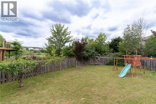 Expansive fenced backyard featuring a manicured lawn, mature trees, and a multi-level wooden deck - 566 Avignon Place, Waterloo, ON 