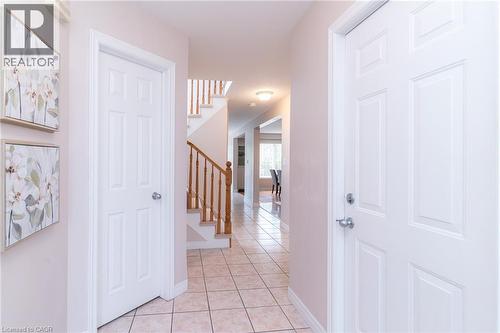 Foyer featuring light-toned square tile flooring, white six-panel doors, and a wood staircase with balusters - 566 Avignon Place, Waterloo, ON 