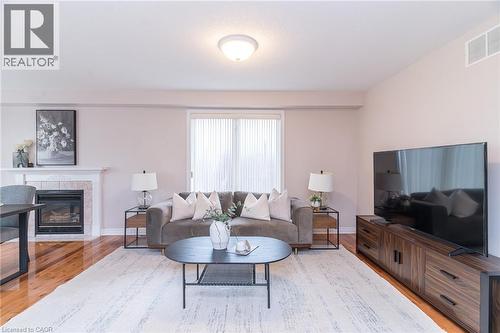 Living area featuring wood-finish flooring, a fireplace with a stone surround and mantel, and a sliding glass door - 566 Avignon Place, Waterloo, ON 