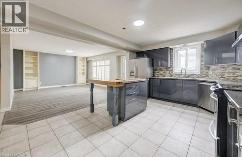 Open-concept kitchen and living area featuring high-gloss gray cabinetry, stainless steel appliances, a center island with wood-finish countertop, and tile flooring - 123 Forest Edge Trail, Kitchener, ON 