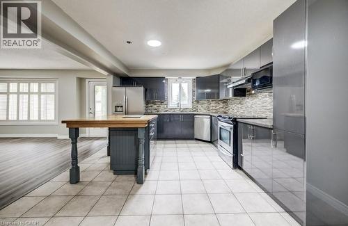 Modern kitchen featuring glossy grey cabinetry, stainless steel appliances, a multi-tone tile backsplash, and a central island with a wood countertop - 123 Forest Edge Trail, Kitchener, ON - Indoor Photo Showing Kitchen