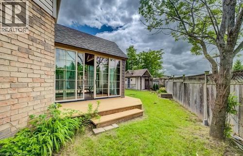 Rear exterior featuring a sunroom with multiple glass panels, an attached wooden deck with steps, a detached shed, a wooden privacy fence, and mature trees - 123 Forest Edge Trail, Kitchener, ON - Outdoor