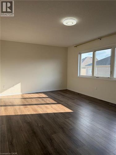Spacious room featuring wood-finish flooring, neutral-toned walls, and a large window with white trim - 235 Apple Hill Crescent, Kitchener, ON 