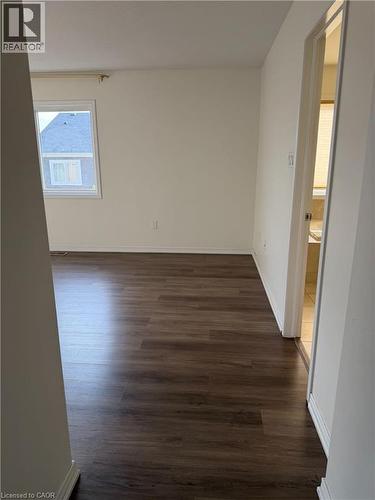 Spacious room featuring dark wood-finish flooring, white baseboards, and neutral wall paint - 235 Apple Hill Crescent, Kitchener, ON 
