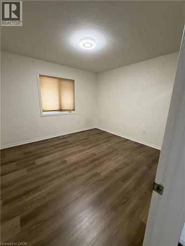 Room featuring wood-finish flooring, a window with horizontal blinds, and a flush-mount ceiling light fixture - 235 Apple Hill Crescent, Kitchener, ON 