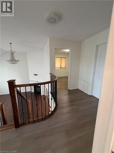 Upper level hallway featuring wood-finish flooring, a rounded dark wood banister with black wrought iron spindles, a light-colored interior door, and white painted walls - 235 Apple Hill Crescent, Kitchener, ON 