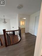 Upper level hallway featuring wood-finish flooring, a rounded dark wood banister with black wrought iron spindles, a light-colored interior door, and white painted walls - 