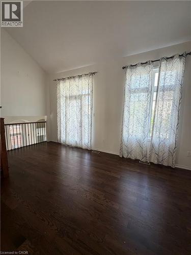 Spacious room with dark wood-finish flooring, two large windows, and a vaulted ceiling - 235 Apple Hill Crescent, Kitchener, ON 
