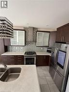 Modern kitchen featuring dark wood-finish cabinetry, light speckled countertops, a stainless steel gas range with a matching range hood, and a dual-basin stainless steel sink - 