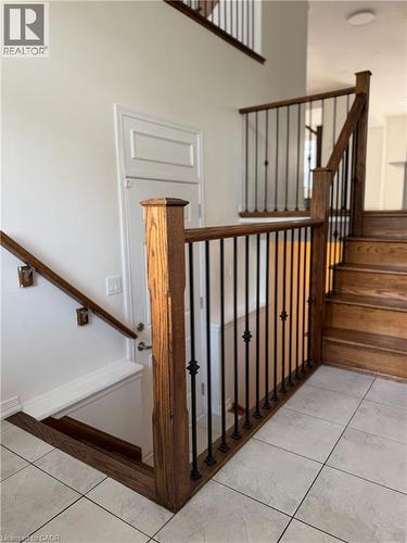 Entryway featuring light-toned tile flooring, a wood staircase with dark iron balusters, and a paneled door - 235 Apple Hill Crescent, Kitchener, ON 