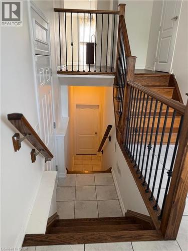 Hardwood staircase with wrought iron balusters leading to a tiled landing - 235 Apple Hill Crescent, Kitchener, ON 