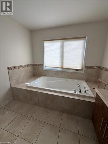 Built-in soaking tub with deck-mounted fixtures, surrounded by neutral-toned tile - 235 Apple Hill Crescent, Kitchener, ON 