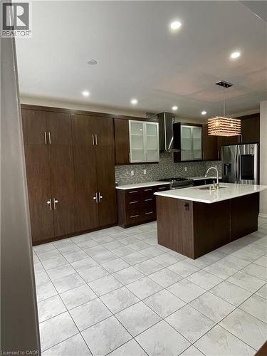 Contemporary kitchen featuring dark wood-finish cabinetry, a large center island with a white countertop, a mosaic tile backsplash, a stainless steel refrigerator, and recessed lighting - 235 Apple Hill Crescent, Kitchener, ON 