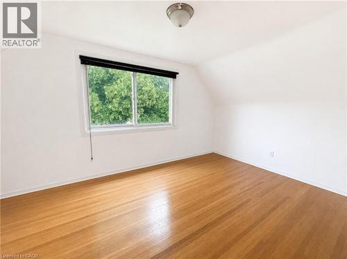 Light-filled room featuring wood-finish flooring, white baseboards, and a window with a black roller shade - 83 East 41St Street, Hamilton, ON - Indoor Photo Showing Other Room