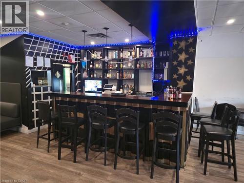 Commercial bar area featuring wood-finish flooring, a full-service bar with built-in shelving, recessed ceiling lighting, and decorative wall accents - 30 Ontario Street S, Kitchener, ON 